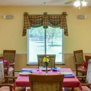 A cozy dining room with tables and chairs neatly arranged by a window with decorative curtains.