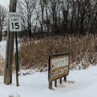 A snow-covered landscape featuring a speed limit sign of 15 mph and a wooden sign partially obscured by snow.
