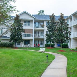 A residential apartment building with a well-maintained lawn and pathway surrounded by trees.