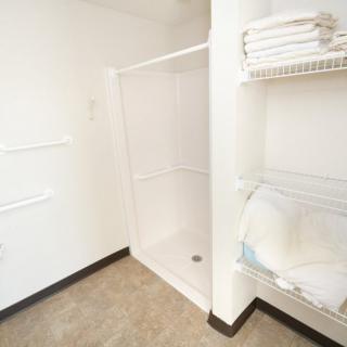 A minimalist bathroom featuring a walk-in shower and neatly stacked towels on shelves.