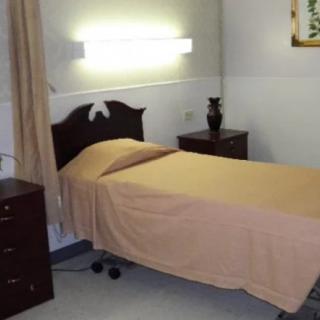 A minimalist room with a single bed and bedside table, possibly in a healthcare setting.