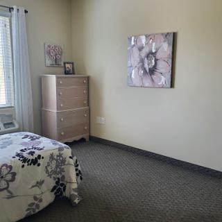 A cozy and simple bedroom featuring a tasteful dresser, decorative wall art, and inviting bedding.