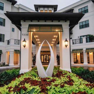 Elegant building entrance with modern sculpture and lush landscaping.