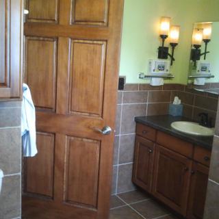 A bathroom featuring a wooden door, sink with mirror, and tiled walls.