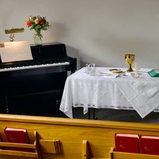 A church setting with a piano, flowers, and an altar table covered with a white cloth.