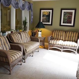 A cozy living room featuring wicker furniture with striped upholstery, complemented by a coffee table, lamp, and framed artwork on the walls.