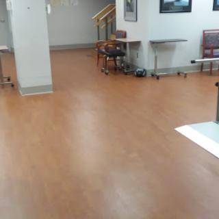 A view of a waiting area in a hospital with wooden flooring and some chairs and tables.