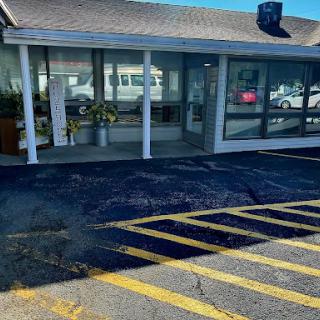 A view of a commercial building with large windows and a striped parking area on a sunny day.