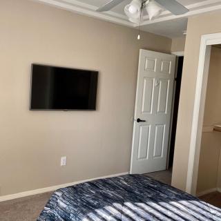 A cozy bedroom featuring a wall-mounted television, an open door, and a ceiling fan.