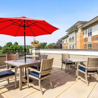 A deck with outdoor seating and a red umbrella near a building surrounded by trees.