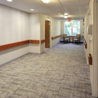 A well-lit hallway in a healthcare facility, featuring a comfortable waiting area with chairs.