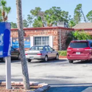 A parking lot in front of a brick building with several parked cars and surrounding trees.