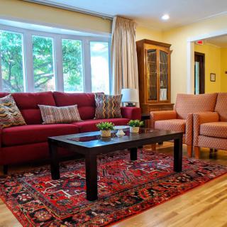 A cozy living room featuring a red sofa, armchairs, and a dark coffee table on a patterned rug.