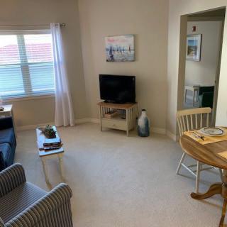 A cozy living room with a TV and seating area, featuring light-colored furniture and decor.
