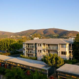 A scenic view of a residential building surrounded by lush greenery and hills in the background.