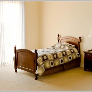 A minimalist bedroom with a single bed, nightstand, and lamp by a window.