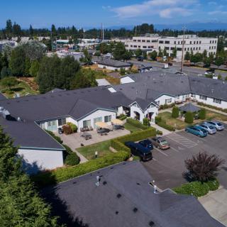 Aerial view of a suburban residential area with houses, trees, and a parking lot on a sunny day.