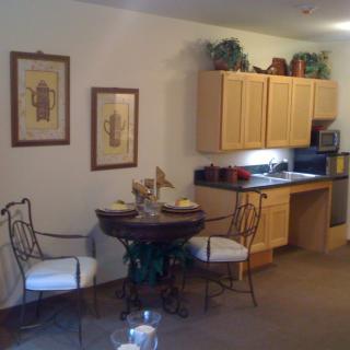 A cozy kitchen and dining area featuring a small table with two chairs, wooden cabinets, and decorative wall art.