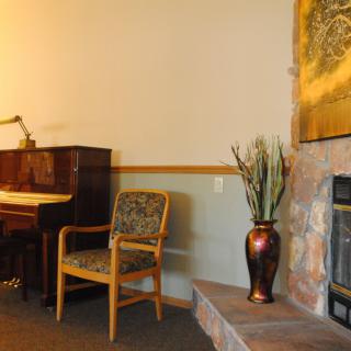 A cozy living room with a piano, chair, and fireplace adorned with a decorative vase.