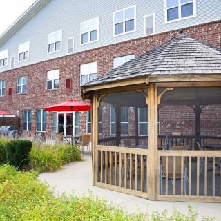 A well-maintained brick building with a wooden gazebo and outdoor seating area featuring red umbrellas.