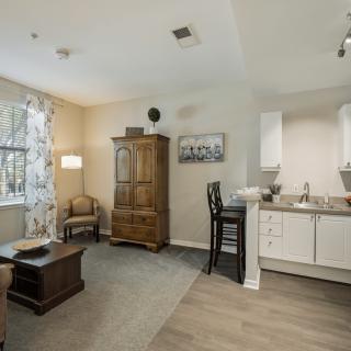 A cozy apartment living space featuring a small kitchen, wooden furniture, and a comfortable armchair by the window.