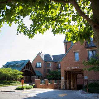 A sunny day outside a large brick building with trees and greenery.