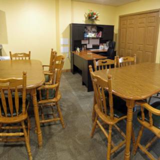 An office space with wooden tables and chairs, featuring a desk in the background.