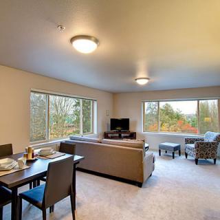 A spacious living and dining area with large windows allowing natural light, featuring modern furniture in neutral tones.