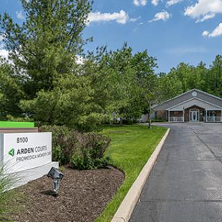 A building with a driveway and a sign, surrounded by trees under a blue sky.