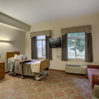 A well-lit hospital room featuring a patient bed, television, and windows for natural light.