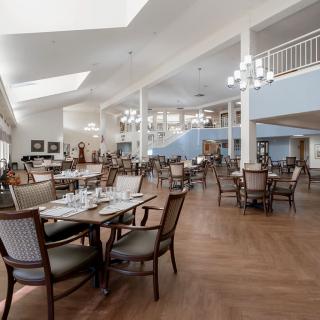 A spacious restaurant dining area with elegant chandeliers and neatly arranged tables and chairs on a wooden floor.
