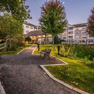 A serene outdoor pathway with benches and trees leading to a multi-story building.