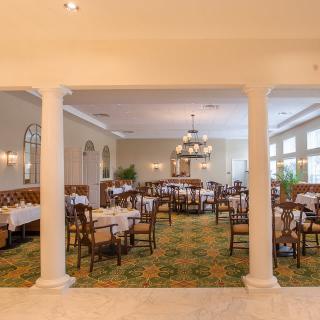 An elegant restaurant dining room with neatly arranged tables and chairs, featuring a chandelier and soft lighting.