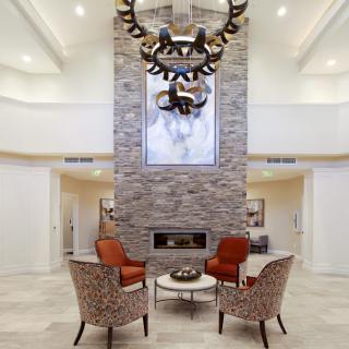 A modern living room features a central stone fireplace, elegant chandelier, and comfortable seating arrangement.