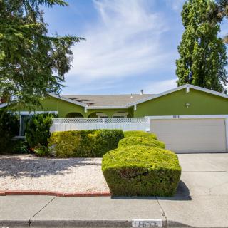 A suburban house with a green exterior, well-maintained front yard, and a two-car garage.