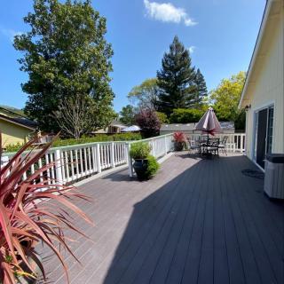 A spacious outdoor deck with patio furniture, surrounded by trees and plants on a sunny day.