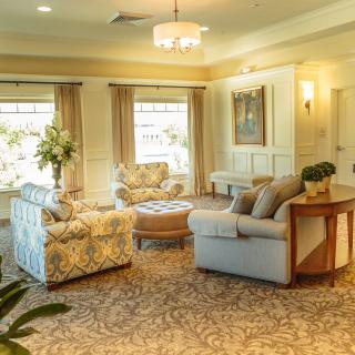 A warmly lit, elegantly decorated living room featuring plush sofas, a carpeted floor, and large windows with curtains.