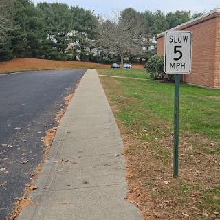 A speed limit sign indicating a maximum speed of 5 mph in a residential area, alongside a concrete sidewalk.