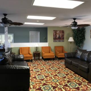 A cozy lobby with a mix of orange chairs and dark sofas, complemented by a colorful patterned carpet and ceiling fans.