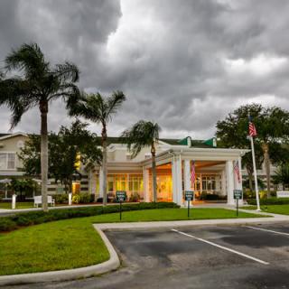 A well-lit building entrance with palm trees under a cloudy sky.