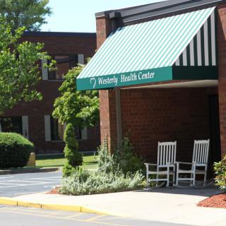 A health center entrance with a green and white striped awning and two rocking chairs.