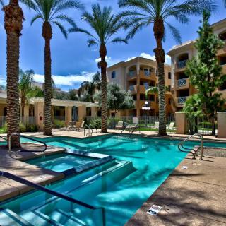 A luxurious resort-style apartment complex featuring a sparkling swimming pool surrounded by palm trees.