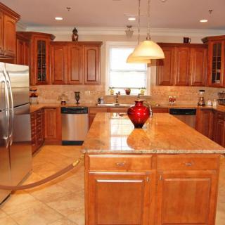 A spacious kitchen featuring wooden cabinets, a central island with a red vase, stainless steel appliances, and pendant lighting.