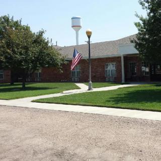 A brick building with an American flag, surrounded by a lawn and trees, with a water tower in the background.