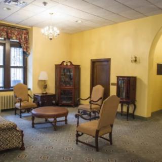 A vintage-style living room with yellow walls, featuring classic wooden furniture and a chandelier.