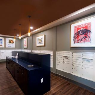 A modern mail room featuring sleek design with wall-mounted artwork and a row of white mailboxes.