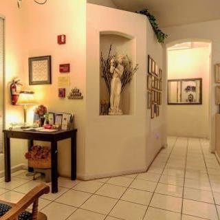 A warmly lit hallway with a statue in a niche, framed pictures on the walls, and a small table with assorted items.