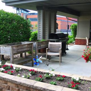 A cozy patio area with seating, a grill, and blooming flowers.