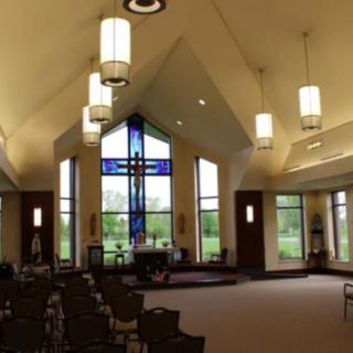 Interior of a church with stained glass, modern lighting, and empty chairs.