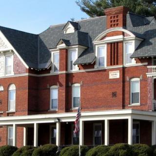 A large historic brick building featuring ornate architectural details and a wraparound porch.
